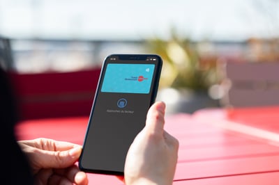 A hand holding a mobile phone with a digital payment card shown on it.