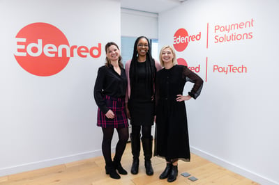 three women shown standing by white walls that show the Edenred logo in red