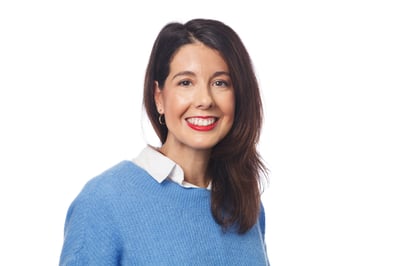 Image shows a woman wearing a blue jumper and buttoned shirt smiling