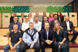 Image shows the Edenred Office break out area with rising seating filled with over a dozen employees; each is sitting and smiling for a group photo. Green dividers are shown in the background.