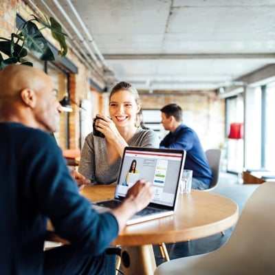 A man and woman enjoying a chat at a cafe, with the woman holding a cup of coffee and the man typing on a laptop